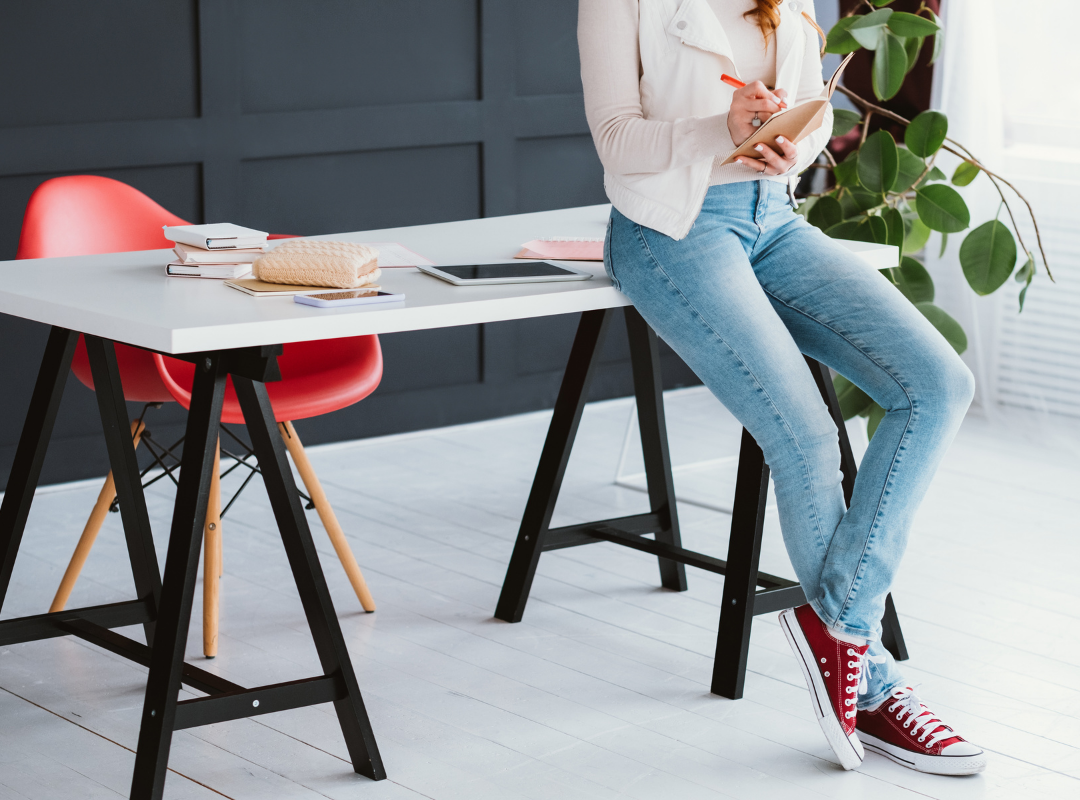 Cropped image of person in white shirt and denim jeans leaning on an 'A' frame desk while looking at her phone